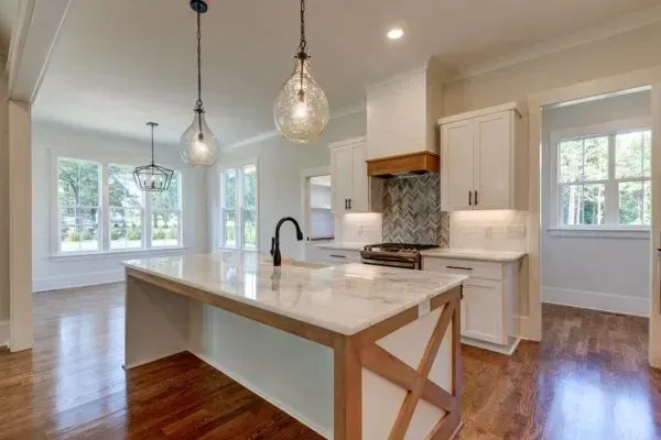 A bright, modern kitchen featuring a marble-topped island with wood accents, white cabinetry, and pendant lighting.