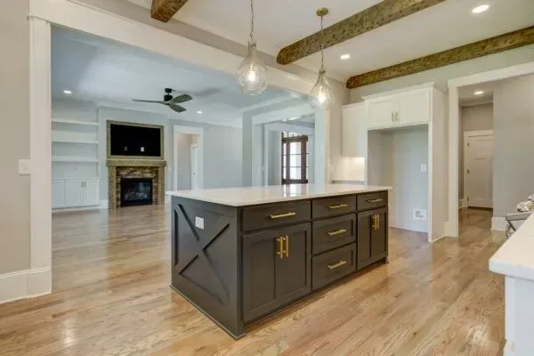 A charcoal kitchen island with gold hardware sits in a bright open-concept home with hardwood floors and wooden beams.