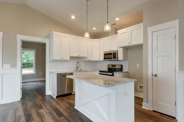 A modern kitchen with white cabinets, stainless steel appliances, a center island, and wood flooring.