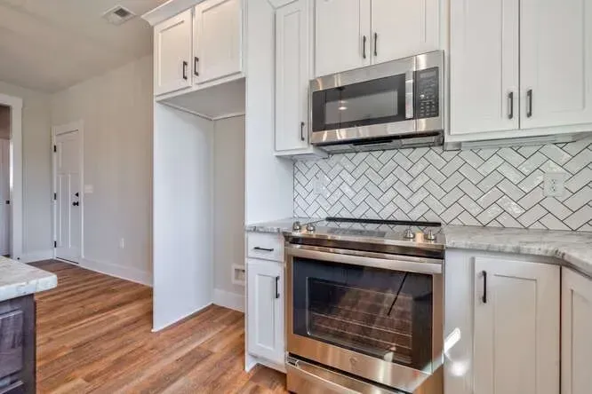 A kitchen featuring white cabinets, a stainless steel oven and microwave, and a white herringbone-tiled backsplash.