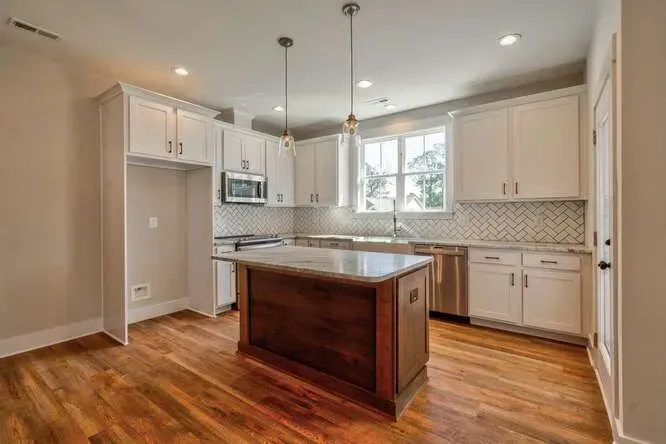 A modern kitchen featuring white cabinets, a dark wood center island, stainless steel appliances, and hardwood floors.