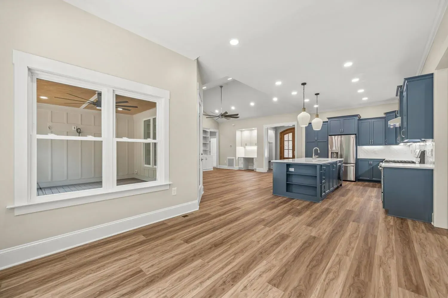 An interior view of a modern kitchen with navy blue cabinets, an island, and wood flooring, seen from an adjacent room.