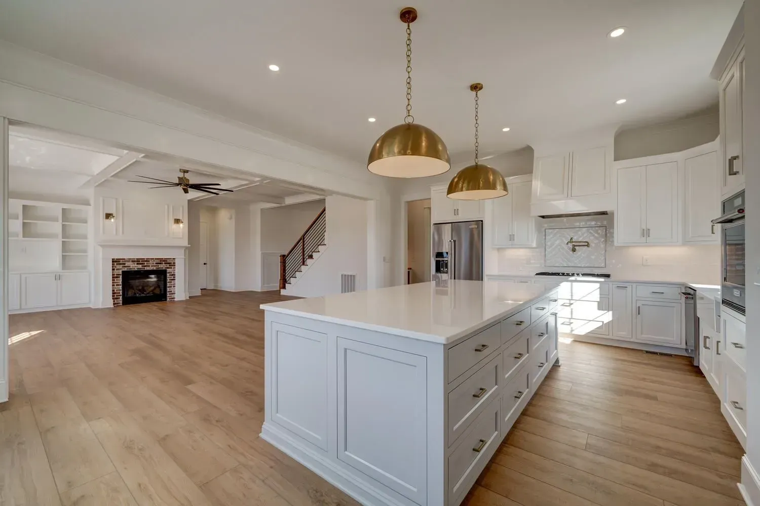 Open-concept kitchen with a light-gray island, quartz countertops, two gold pendant lights, and light wood flooring.