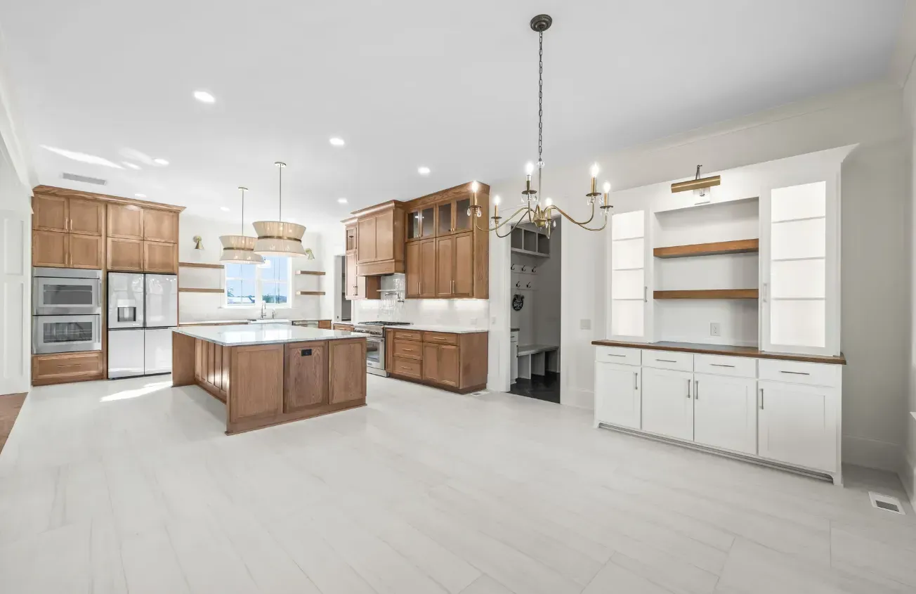 A modern kitchen with wood-toned cabinets, a center island, stainless steel appliances, and a white built-in buffet.