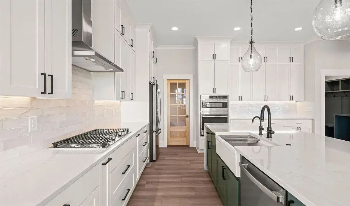 Modern kitchen with white upper cabinets, green lower cabinets, quartz countertops, and wooden flooring.