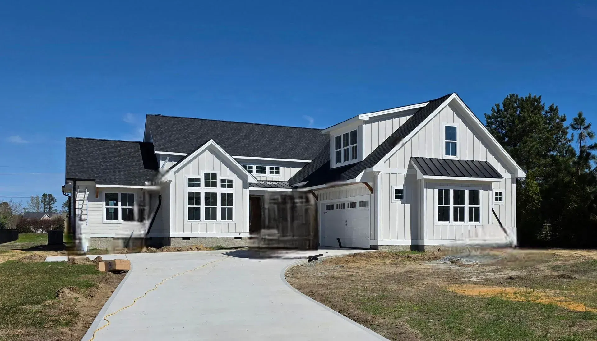 A large, modern white house with board and batten siding, a dark roof, and a concrete driveway under a clear blue sky.