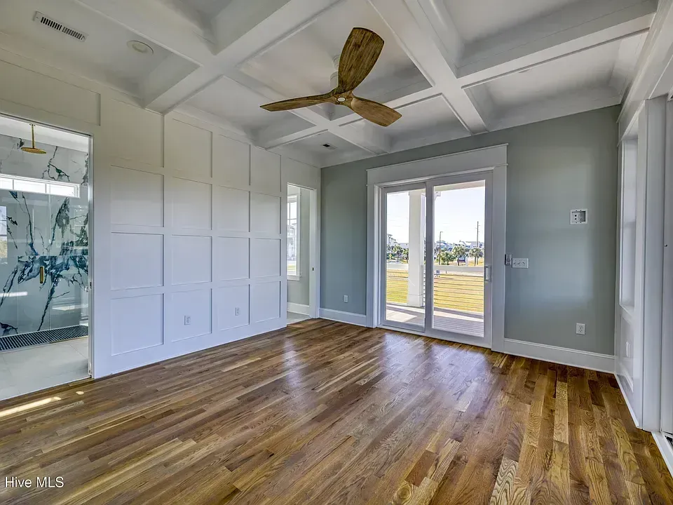 Empty modern bedroom with wood floors, tray ceiling, ceiling fan, and French doors to a balcony.