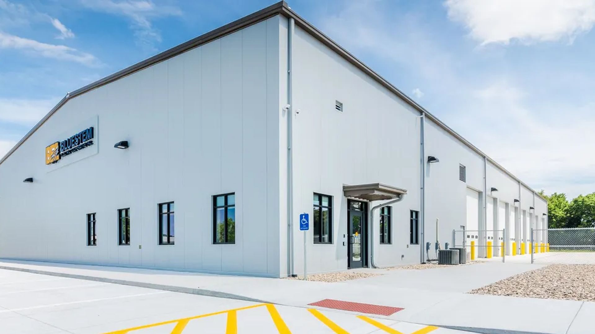 Modern, light-gray industrial warehouse building with multiple roll-up doors, windows, and an ADA entrance on a sunny day.
