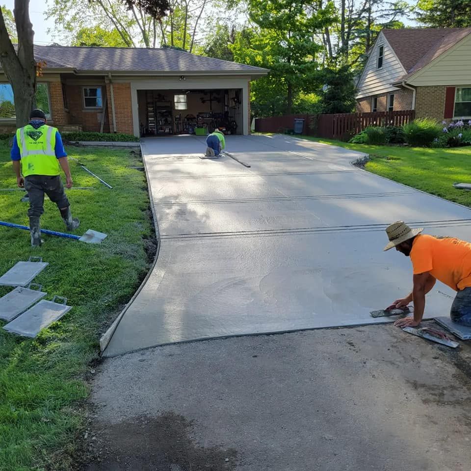 Two men are working on a concrete driveway in front of a house.