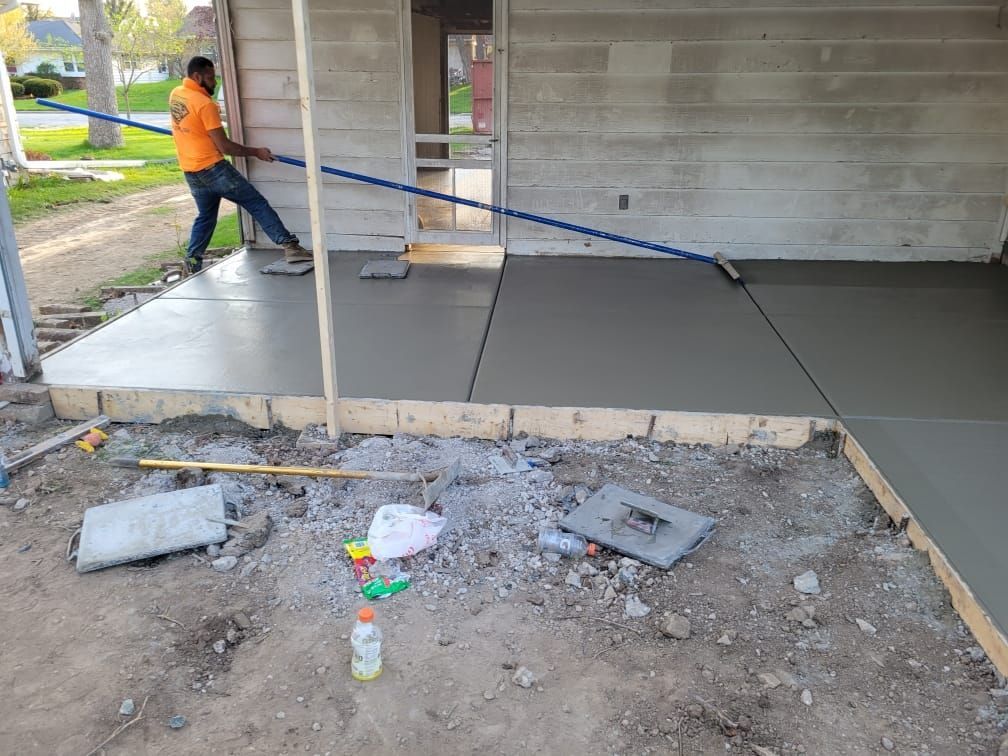 A man is laying concrete on a porch in front of a house.