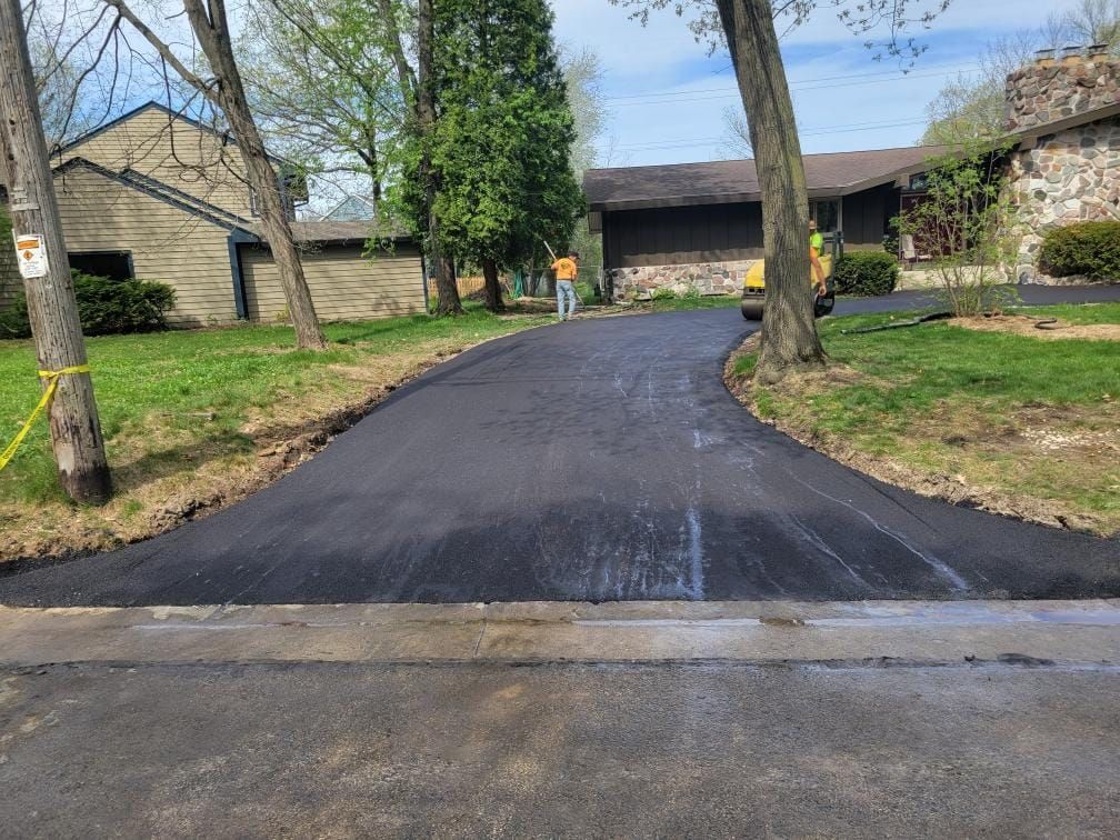 A man is standing on a newly paved driveway in front of a house.
