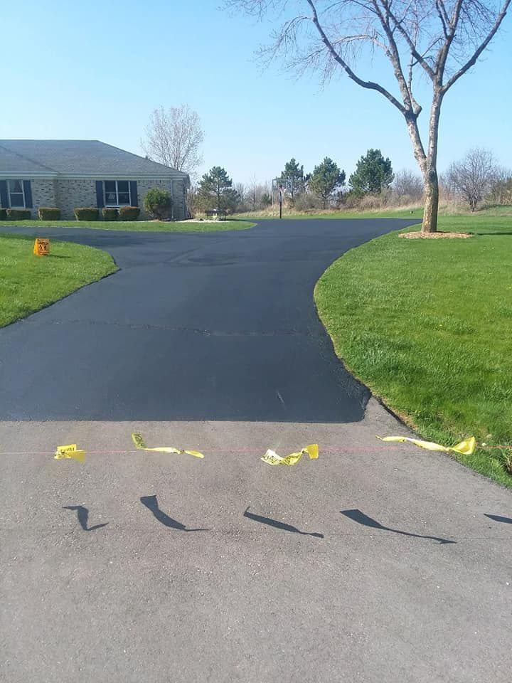 A driveway with a house in the background and a tree in the middle