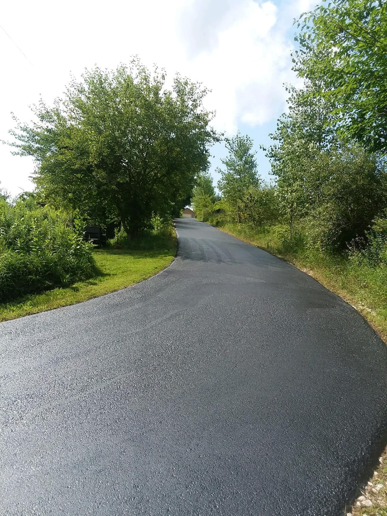 An asphalt road with trees on both sides and grass on the side.