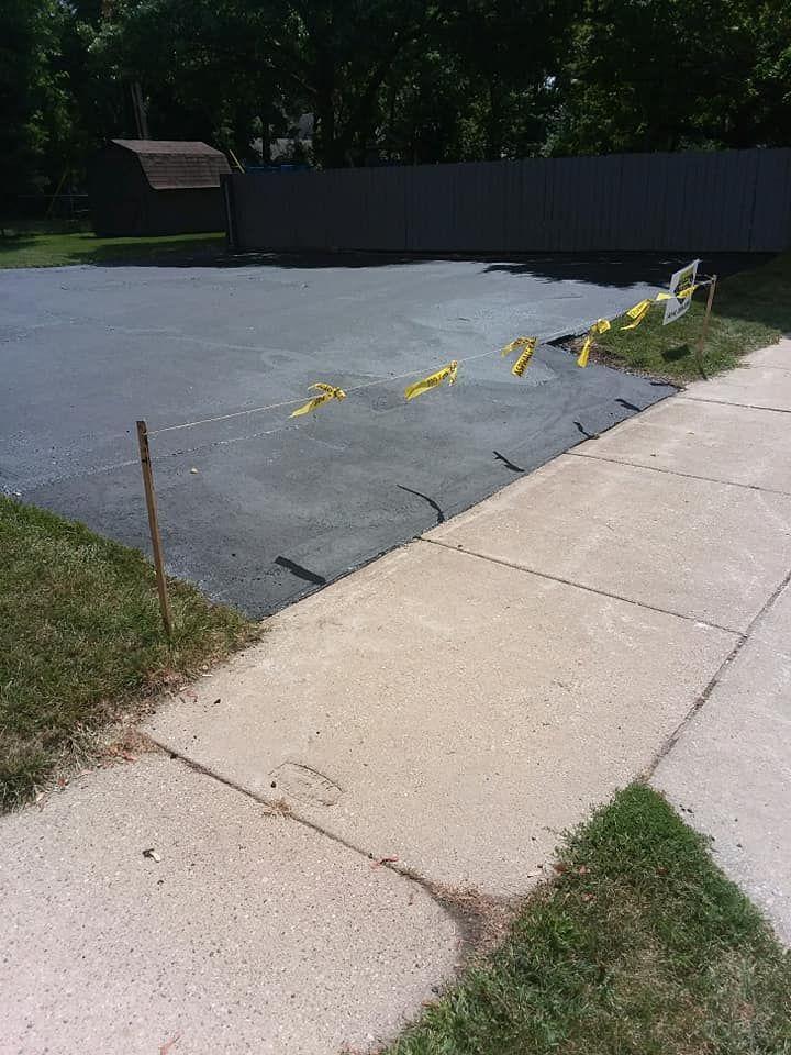 A concrete sidewalk next to an asphalt driveway.