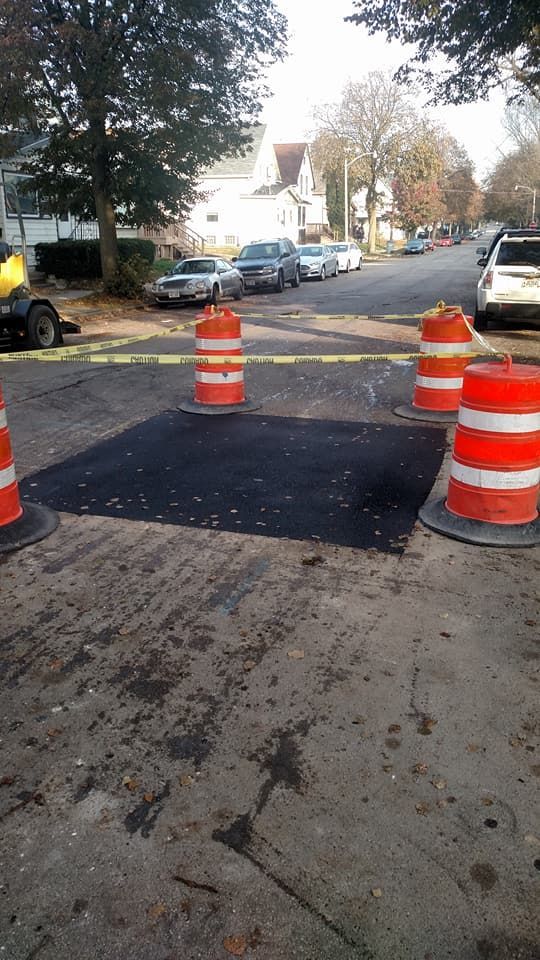 A row of orange and white traffic cones around a patch of asphalt.