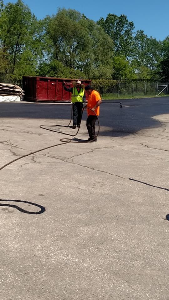 Two men are sealcoating a concrete driveway.