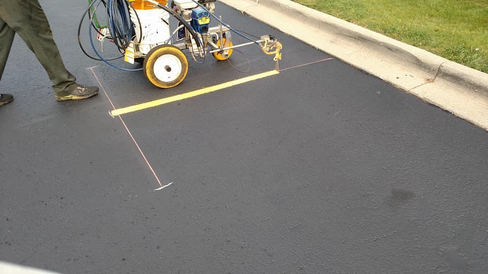 A person is using a machine to paint a yellow line on the road.