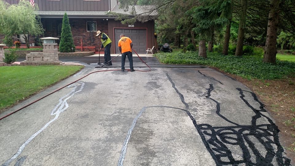 Two men are working on a driveway in front of a house.