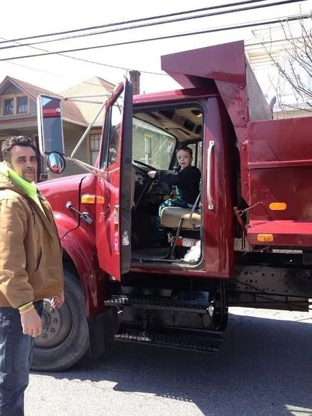 Red dump truck parked roadside with driver’s door open and a man standing beside it