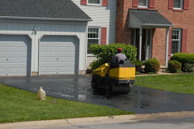 Person washing a yellow lawn mower in a driveway in front of a suburban garage
