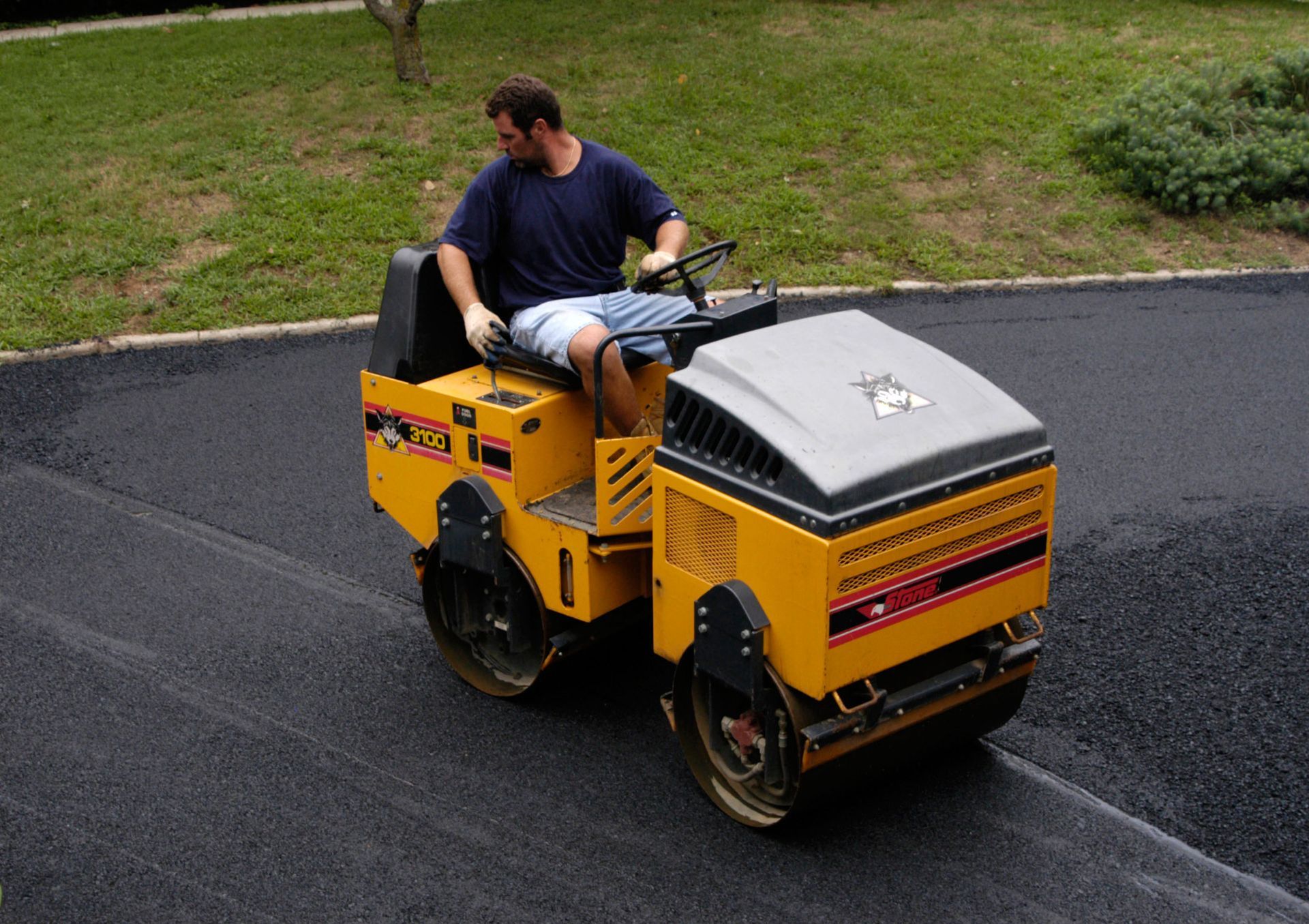Man riding a yellow road roller on freshly paved asphalt outdoors