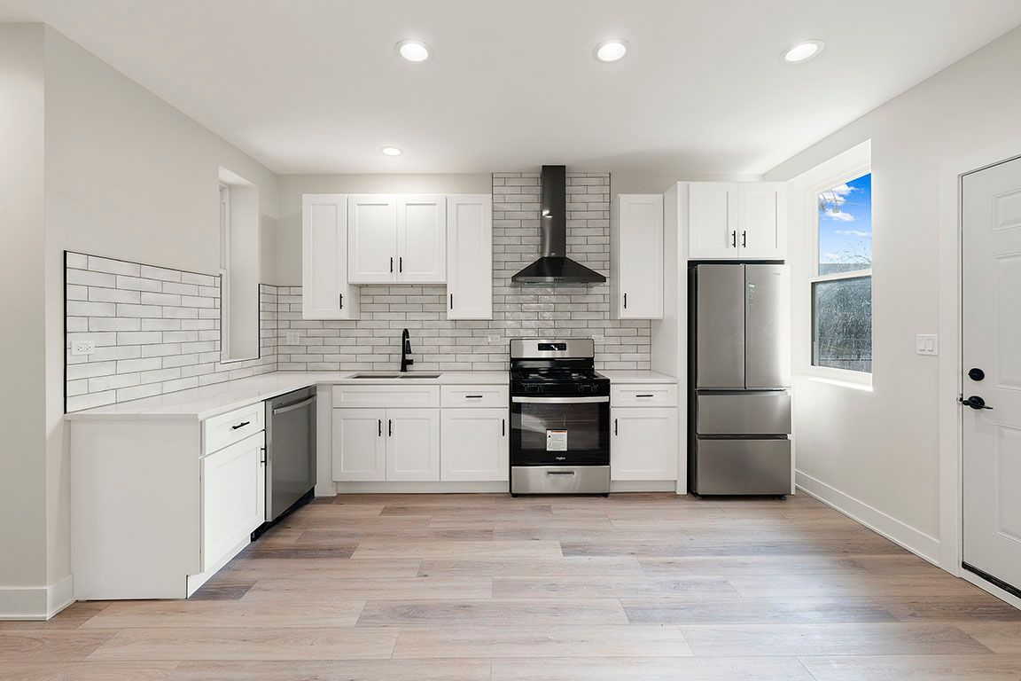 An empty kitchen with white cabinets and stainless steel appliances.