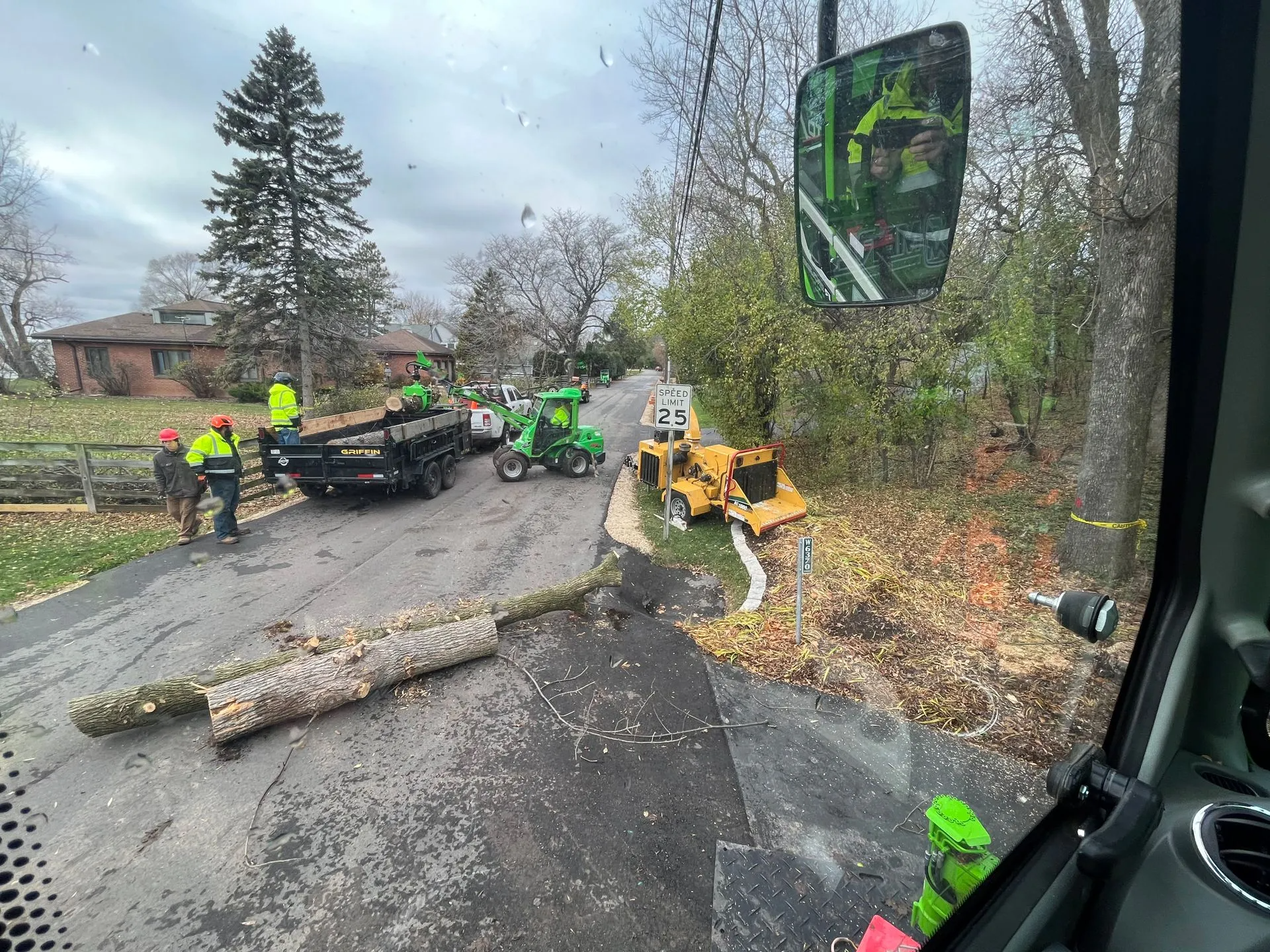 Road crew clearing fallen tree. Workers in safety vests, chipper, truck on road.