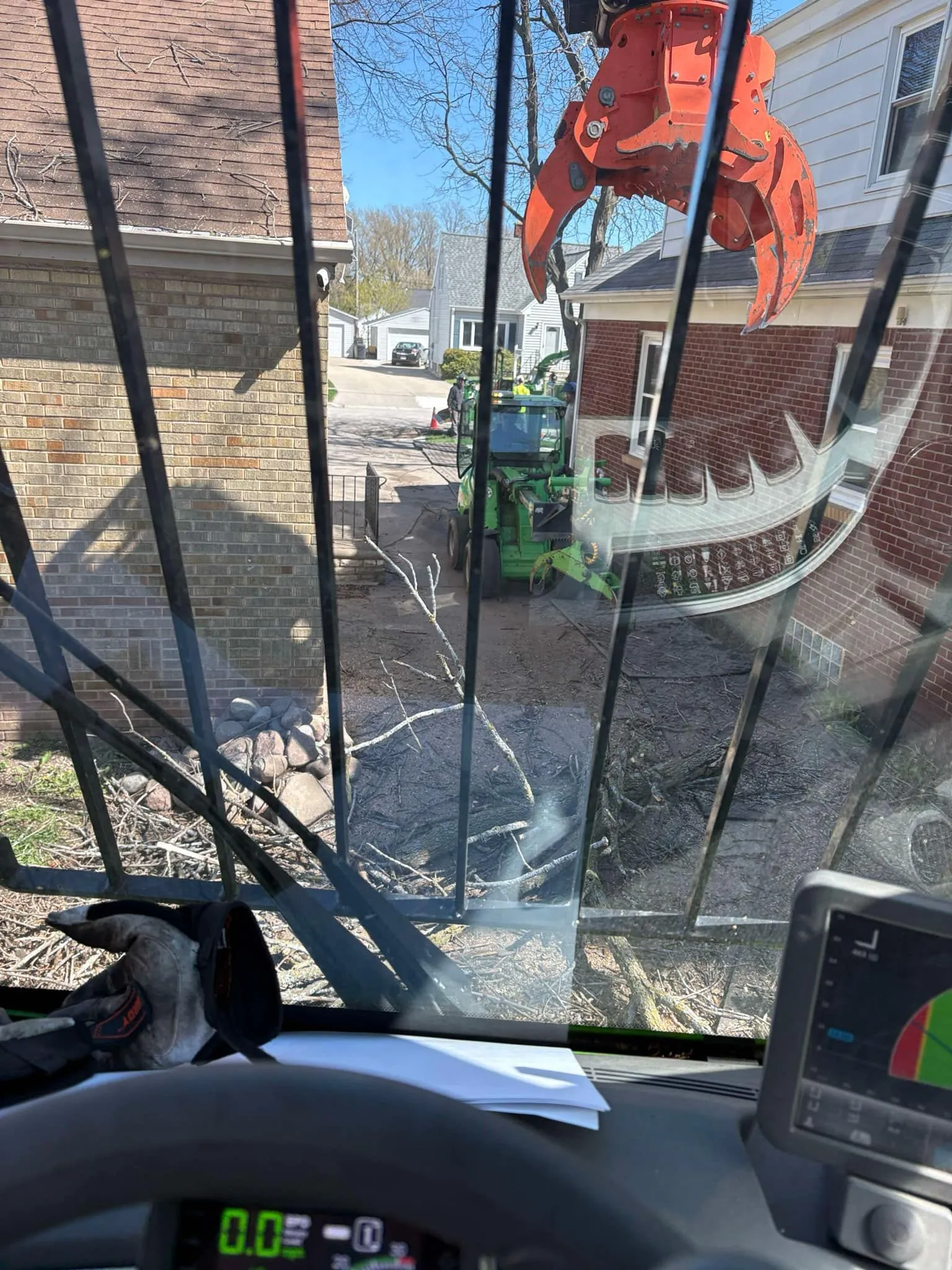 View from inside a machine with a large claw, operating near buildings, streets, and trees.