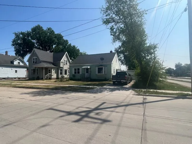 Two-story house and a small house with a pickup truck in the driveway, power lines overhead, sunny day.