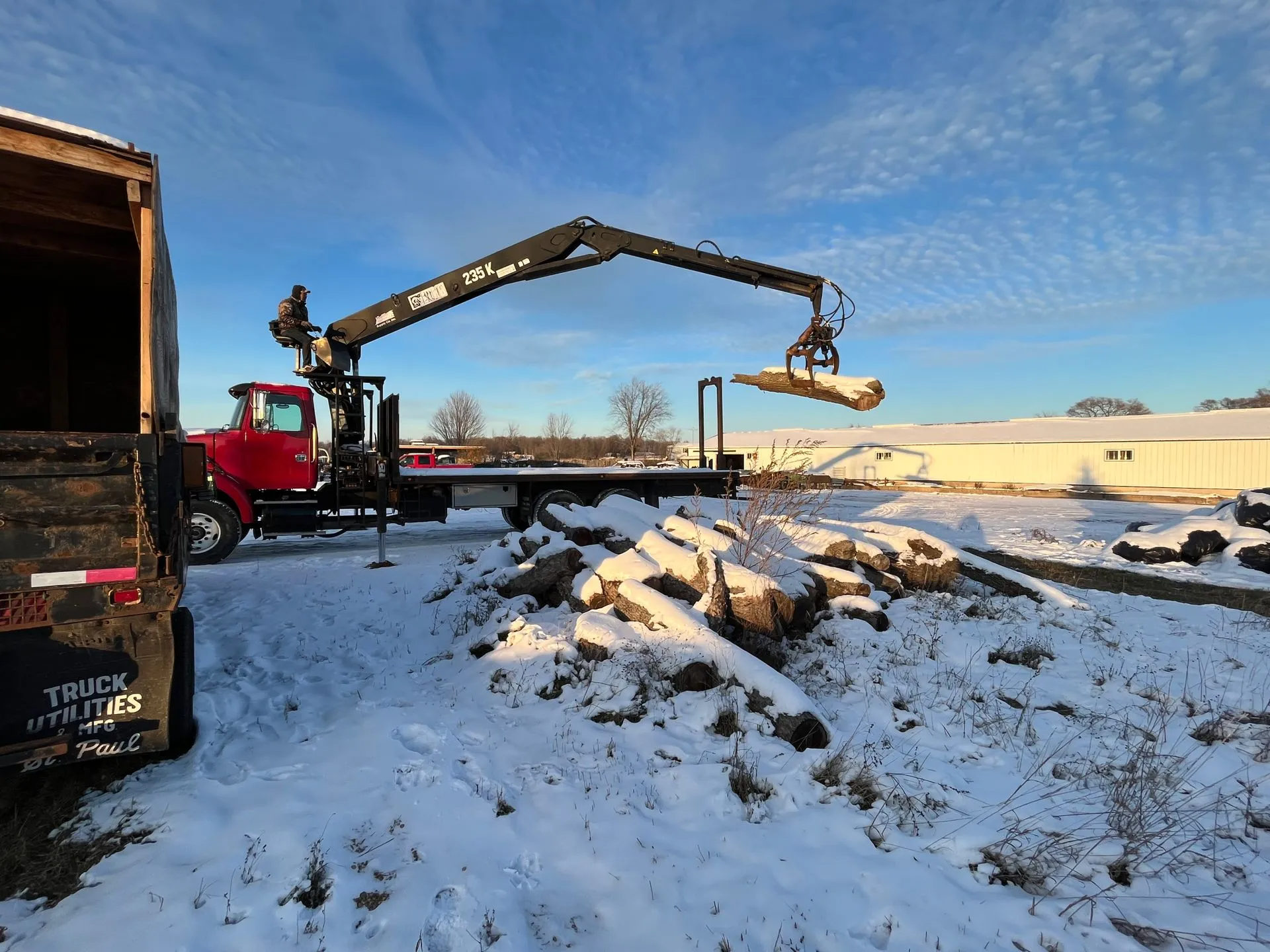 A red truck with a crane is lifting a wooden beam in a snowy outdoor setting.