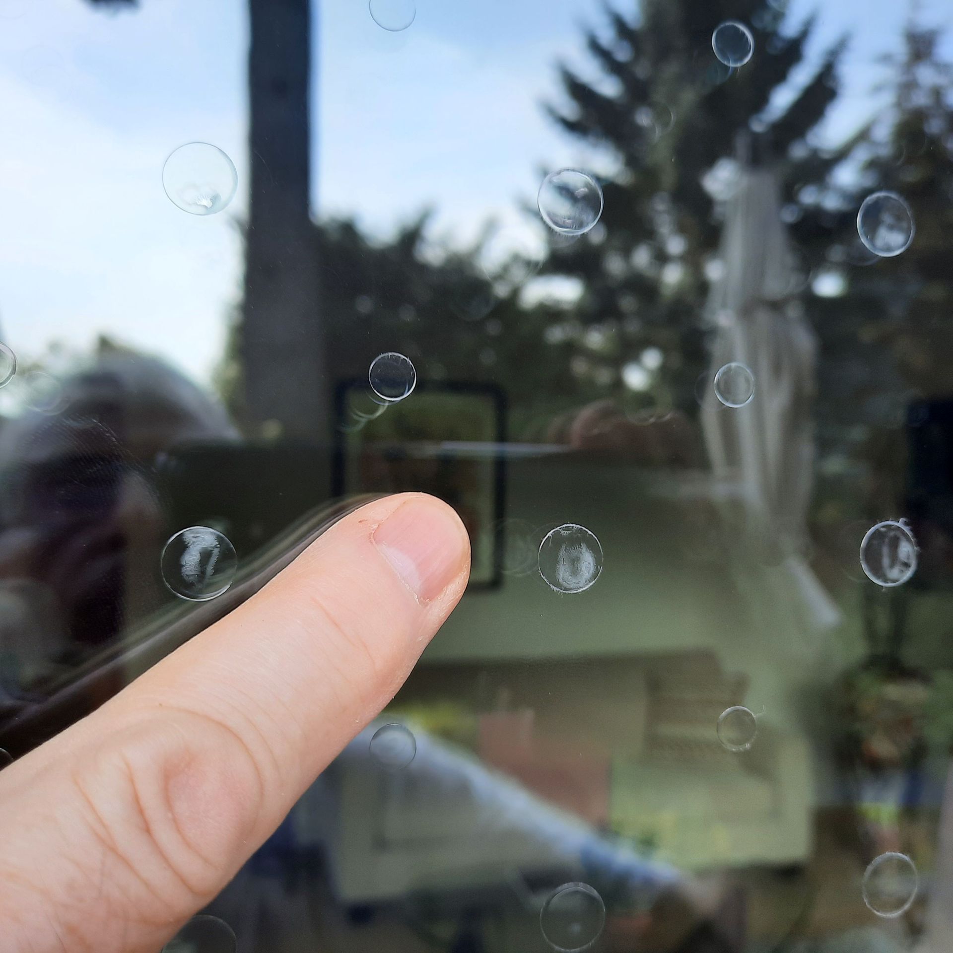 A close-up view of a hand pointing at a clear window marked with a grid of small, circular adhesive stickers.