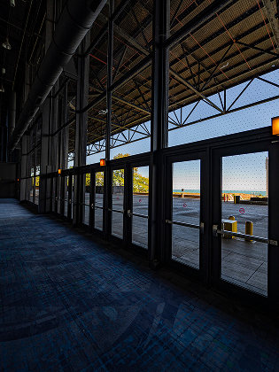 A view from inside a building looking through a row of glass doors toward an outdoor patio overlooking the sea.