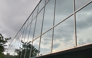 A low-angle view of a modern building's grid-patterned glass facade reflecting a cloudy sky and nearby trees.