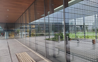A modern building exterior featuring a large glass curtain wall with a subtle white dot pattern, viewed from a patio.