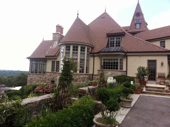 Two-story house with gray siding, white stucco, garage door, and windows. Blue sky overhead.