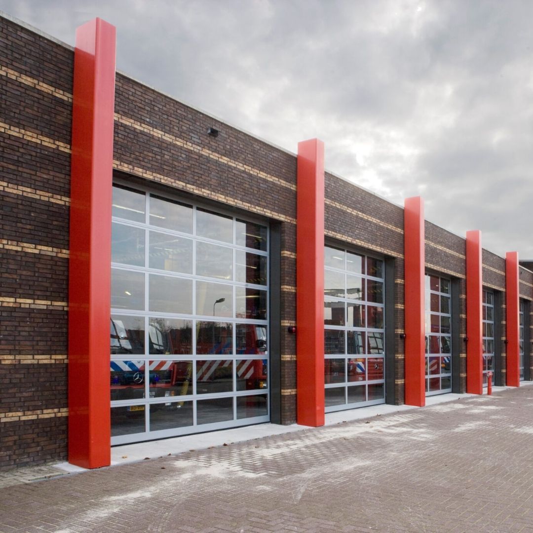 Fire station exterior, brick building with red columns, glass garage doors, and a cloudy sky.