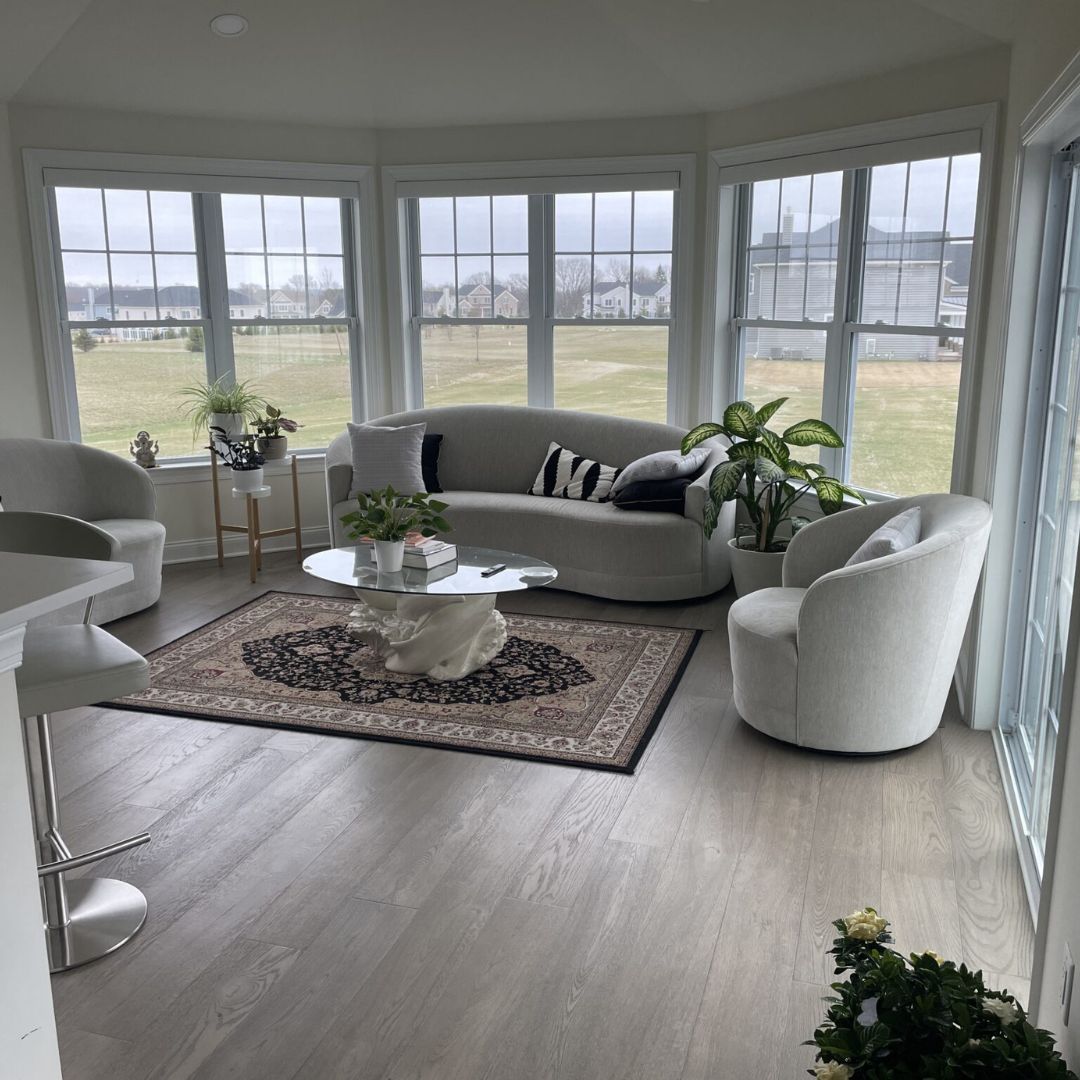 Living room with a curved sofa, two armchairs, and a round coffee table in front of large windows.