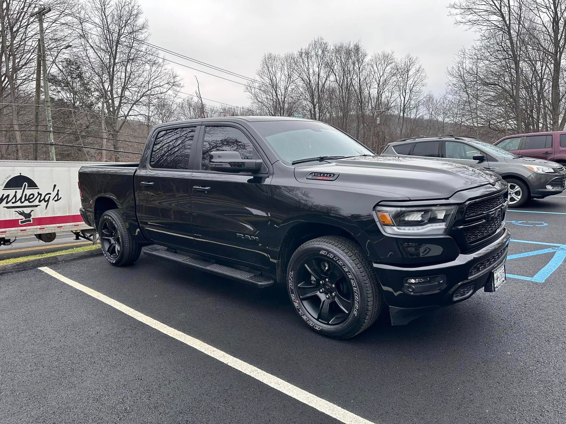 Black Ram pickup truck parked in a lot, near a building with a sign and another car.