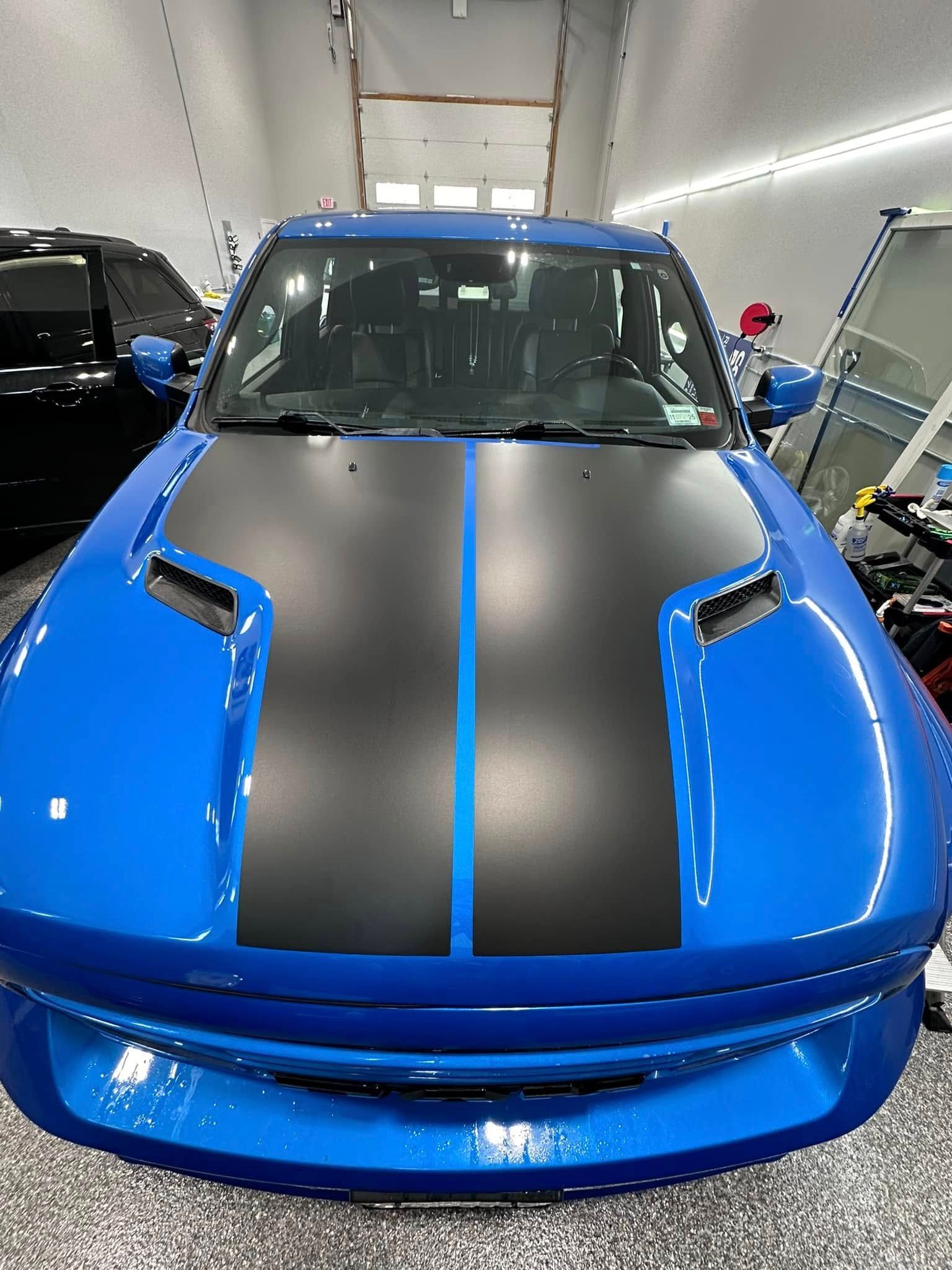 Blue Ford Mustang with black hood stripe, parked in a garage.