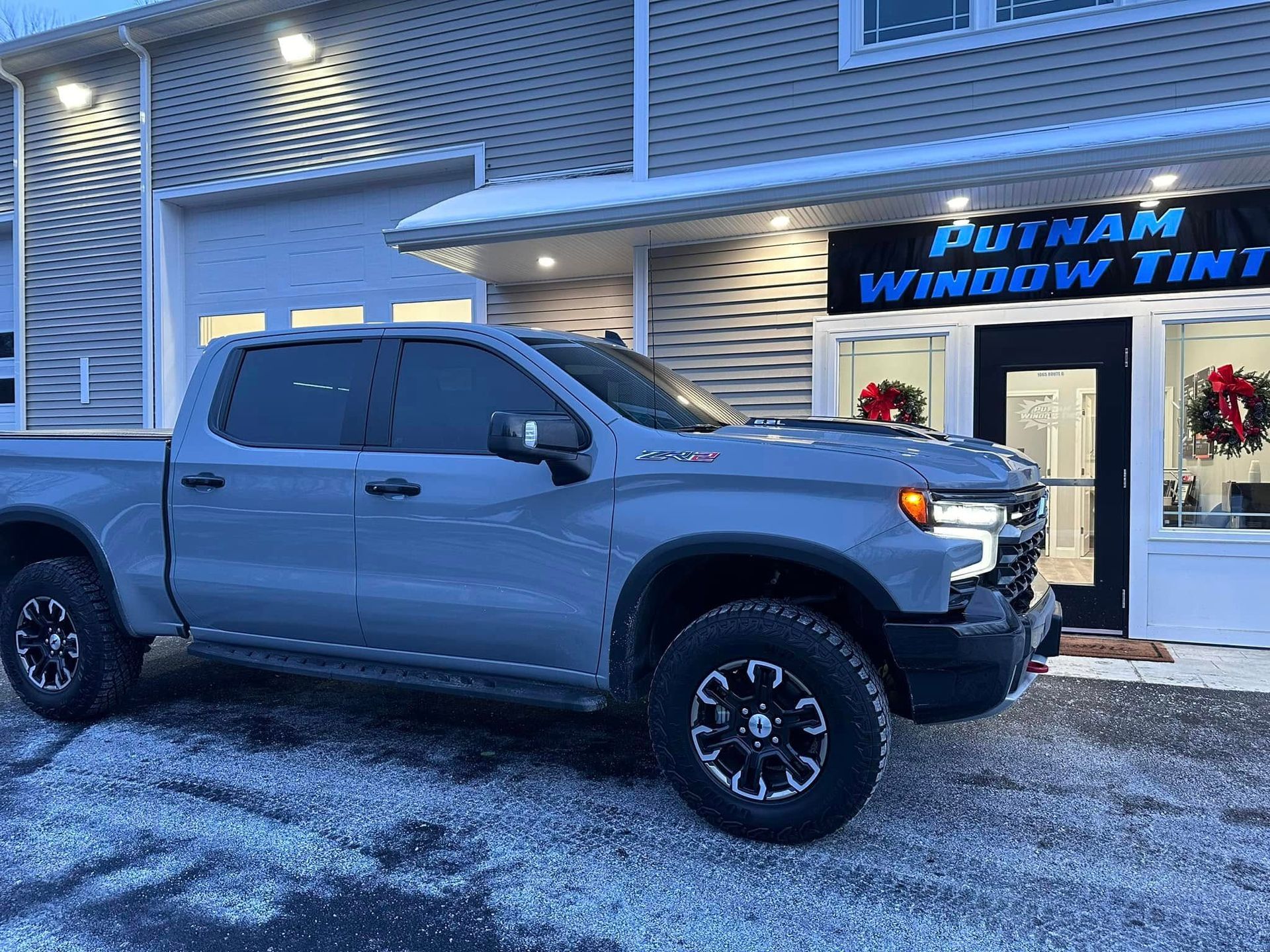 Gray truck parked outside Putnam Window Tint shop. Building with sign and Christmas decorations.