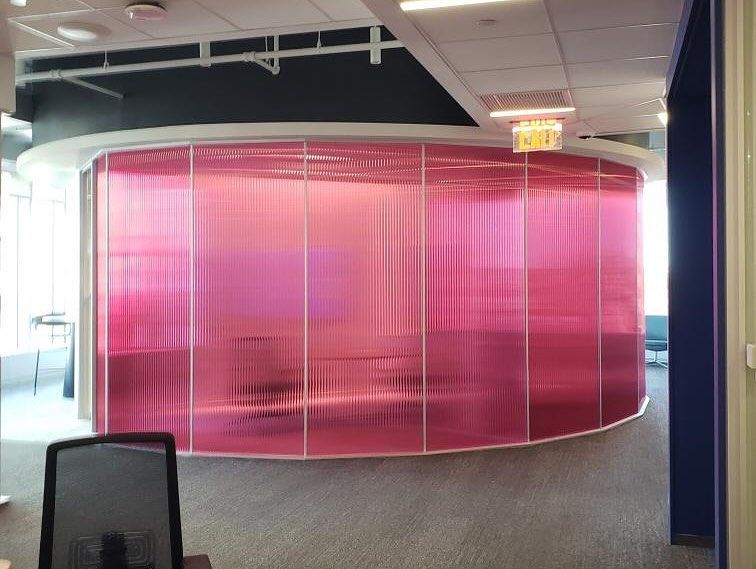 Pink, translucent curved wall in an office space. It has a ridged texture, and is bordered by a white frame.