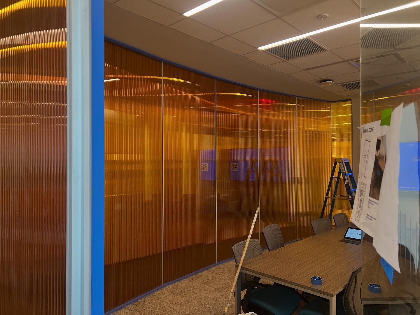 A curved, golden-toned glass wall in an office. A table and ladder are visible.