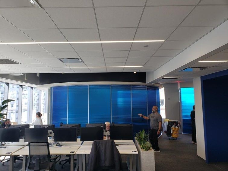 Office interior with workstations, blue wall, man pointing, and people working.