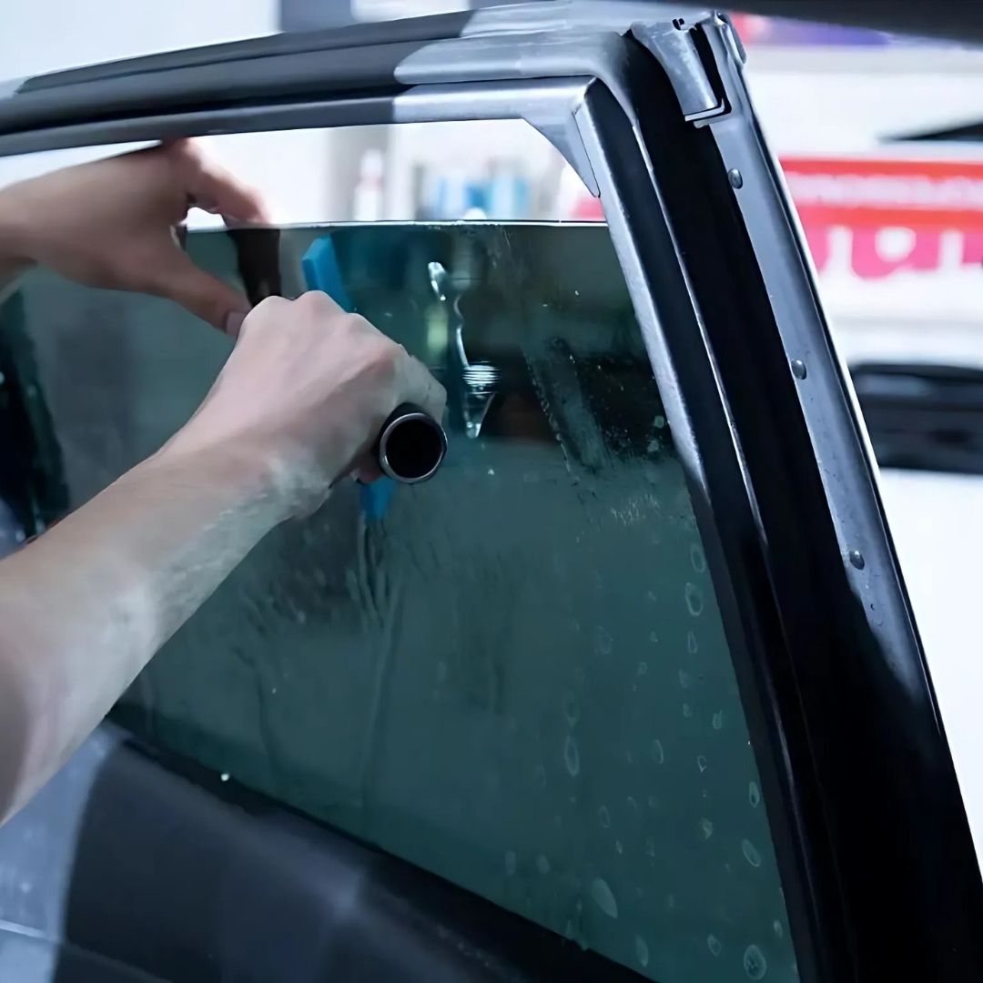 Person applying tinted film to a car window with a squeegee.