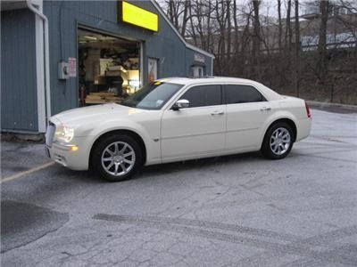 White Chrysler 300 sedan parked in front of a blue garage, likely a car repair shop. Snowy pavement.