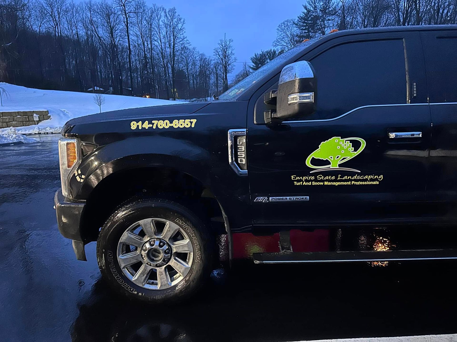 Black truck with company logo and phone number parked outdoors in winter.