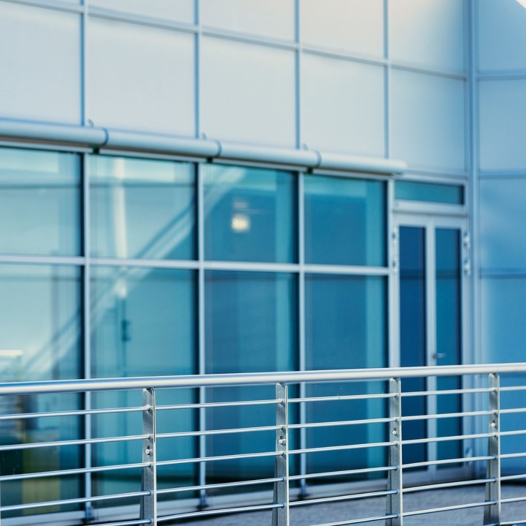 A modern building with large glass windows, a door, and a metal railing.