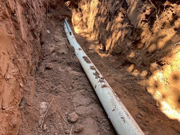 White pipe laid in a dirt trench with muddy soil along the sides.
