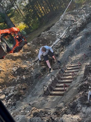 Person climbing a rocky slope beside a rusted ladder near an orange excavator.