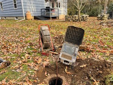 Two utility locators pulled from a hole in a leaf-covered yard, with a house in the background.